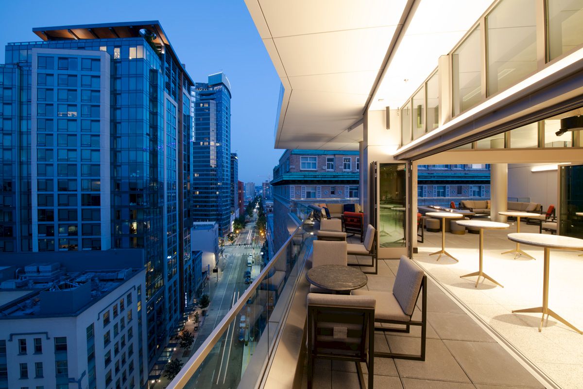 The image features a modern balcony with sleek furniture, overlooking a city skyline at dusk, highlighting urban life.